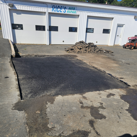 Fresh black asphalt patch in front of an auto repair shop with white garage doors.