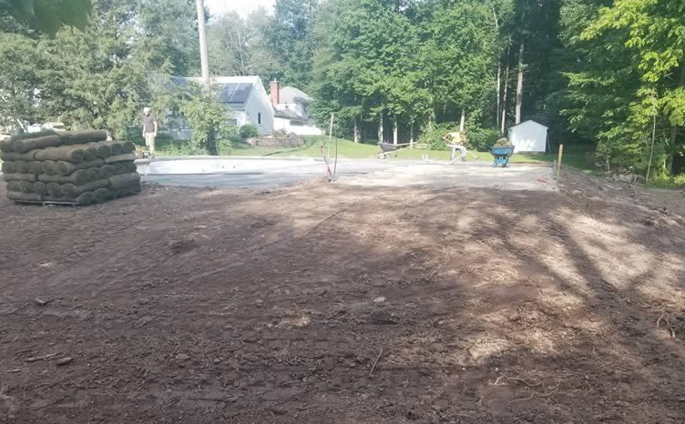 Freshly cleared yard with dirt ground, stacked tires on the left, and trees and houses in the background.