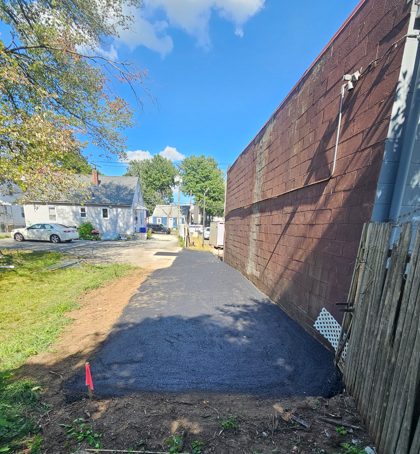 Narrow paved path beside a red brick wall, leading past houses under a blue sky.