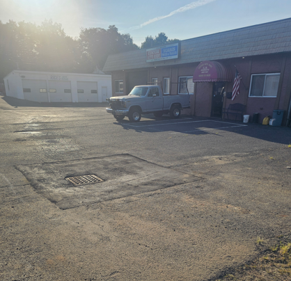 Sunny parking lot outside a small building with a white pickup truck parked near the entrance.