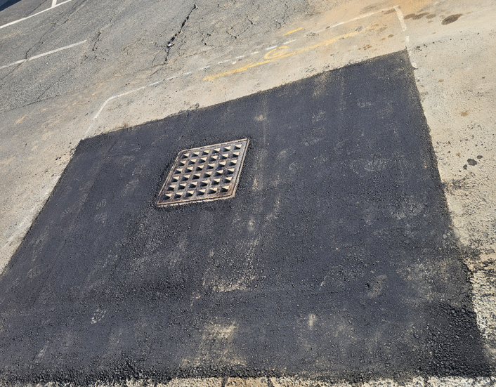 Pavement patch with a square metal drain grate set in dark asphalt