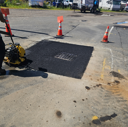 Road repair patch with drain grate, orange cones, and a pavement cutter on a worksite