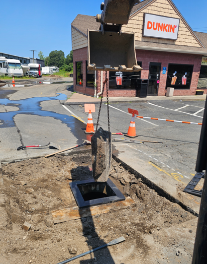 Roadwork trench and cones in front of a Dunkin’ store parking lot.