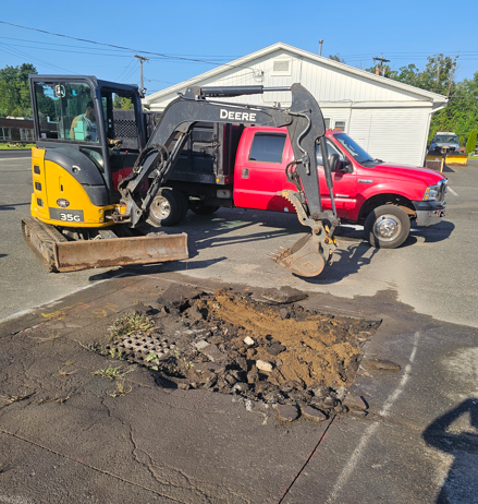 Yellow excavator beside red pickup over broken asphalt at a construction site