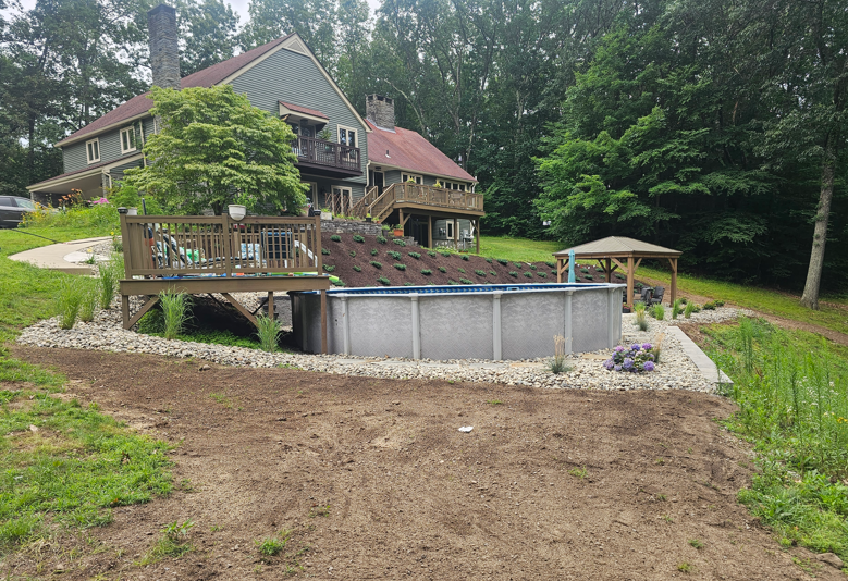 House with wooden deck overlooking an above-ground pool in a wooded backyard