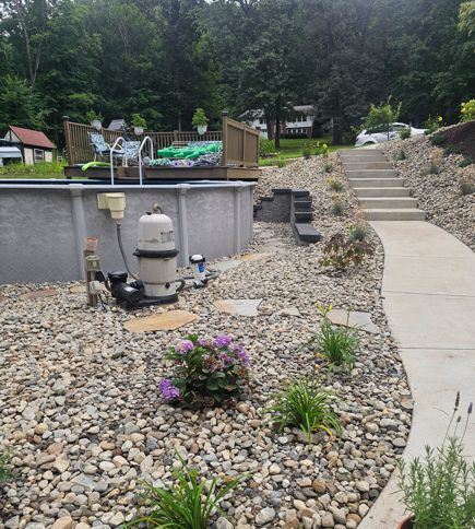 Backyard pool area with stone landscaping, steps, and a concrete walkway beside a hot tub.