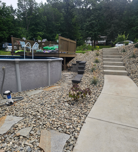 Backyard with curving concrete path, stone steps, retaining wall, and an above-ground pool deck