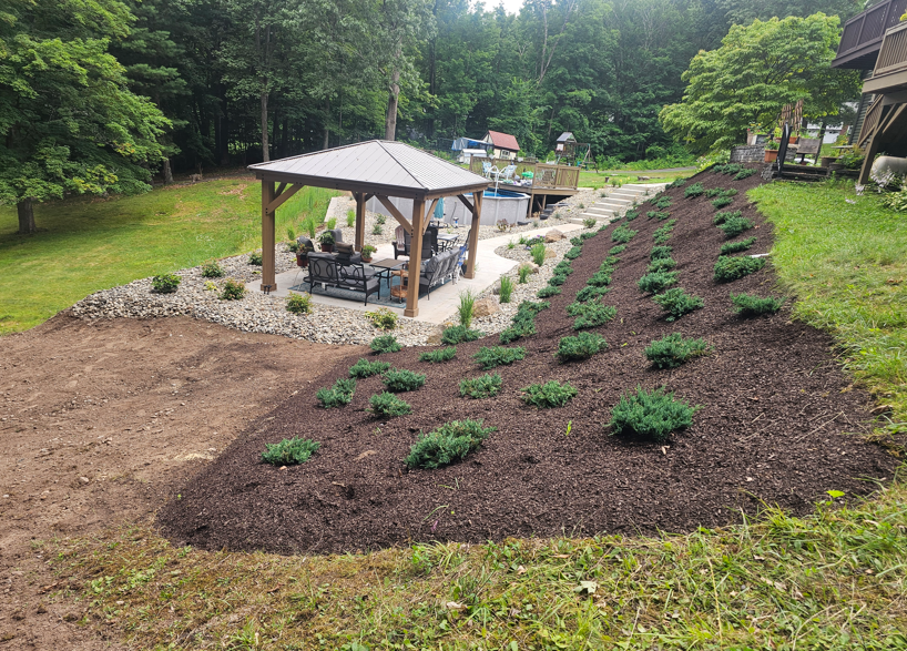 Backyard garden with a gazebo and newly planted shrubs on a mulched hillside.