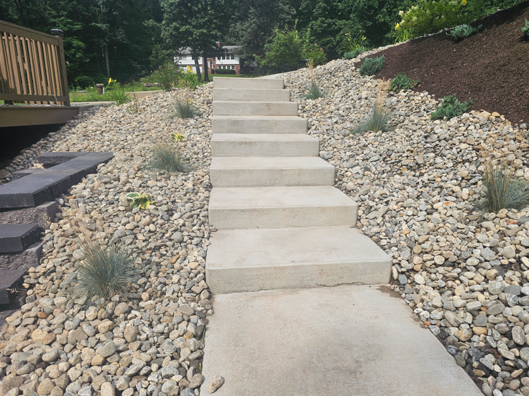 Concrete steps up a landscaped gravel slope beside a wooden deck and shrubs