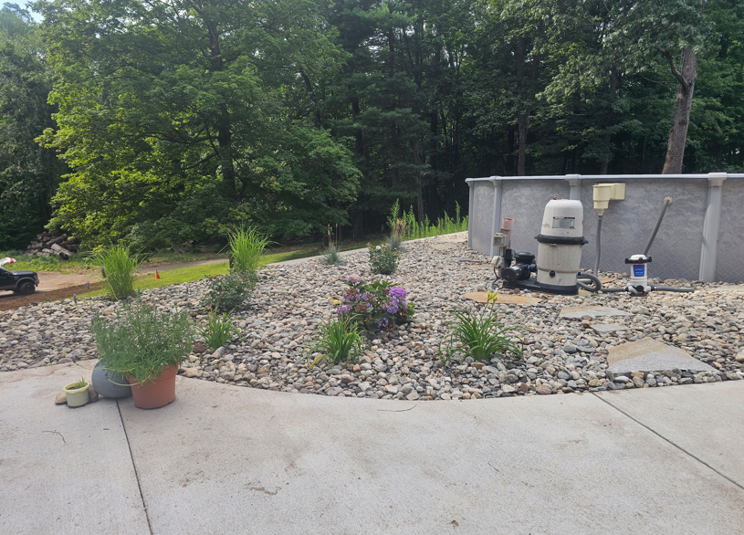 Concrete patio beside a rock garden with potted plants, shrubs, and a wooded background