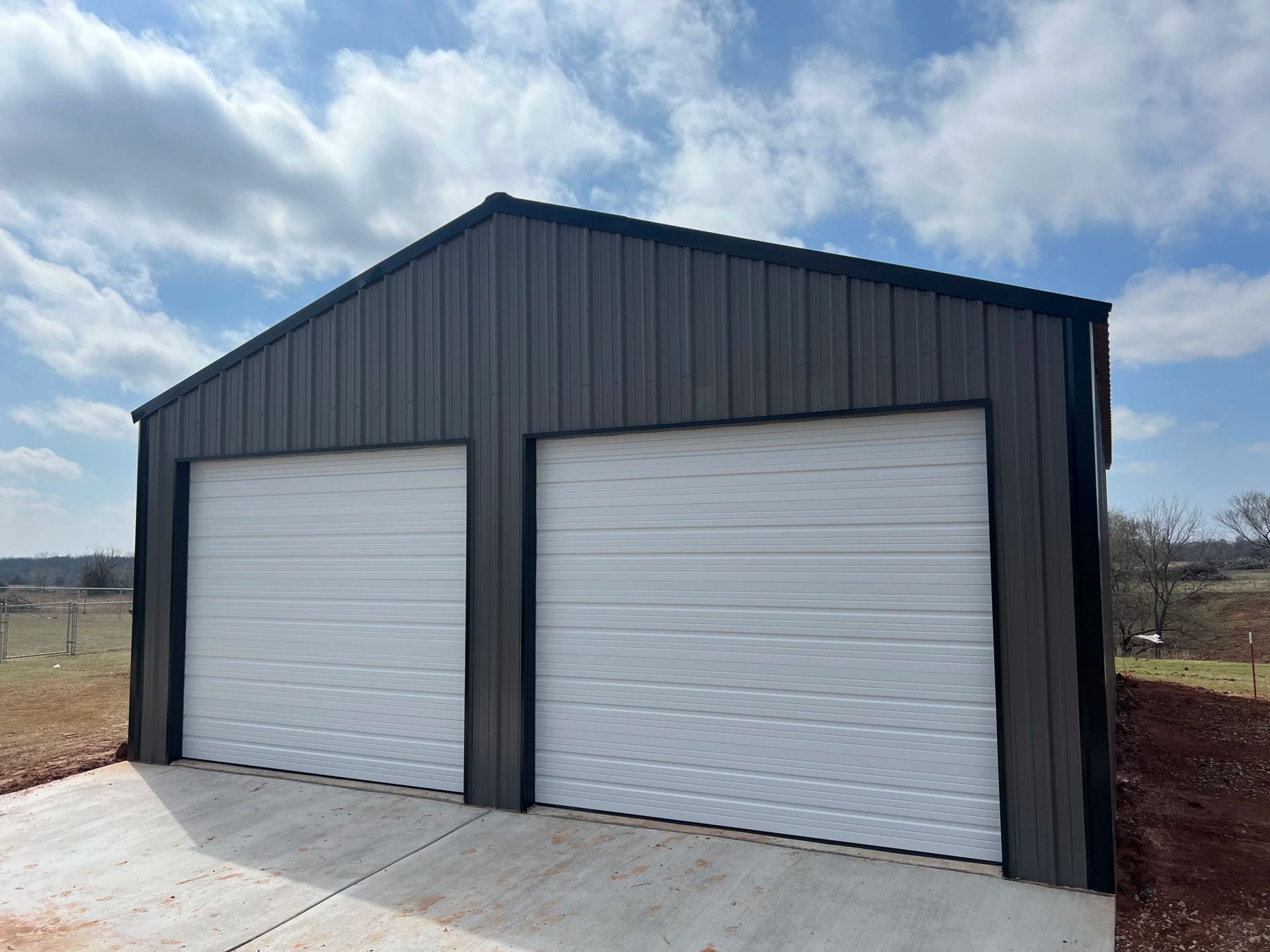 Dark metal two-car garage with white roll-up doors under a cloudy sky