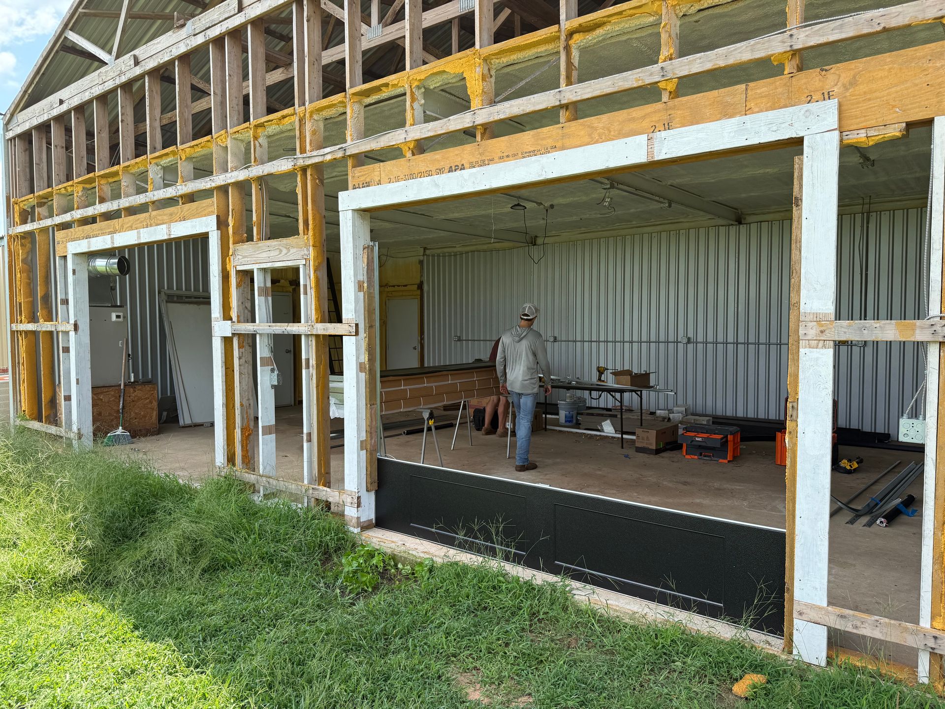 Partially built house exterior with open framing and a worker standing inside a large doorway.