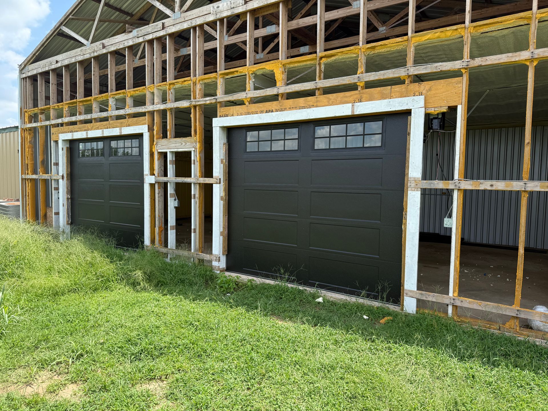 Partially built structure with two black garage doors and exposed framing under construction