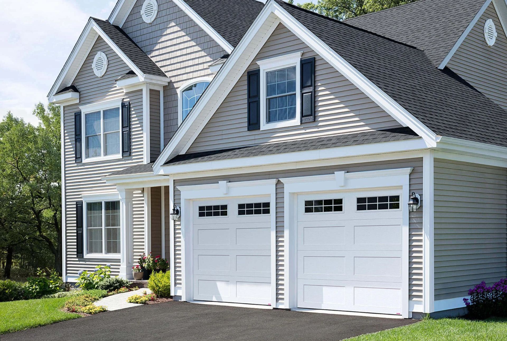 Suburban house with gray siding, white trim, and a two-car garage in bright daylight