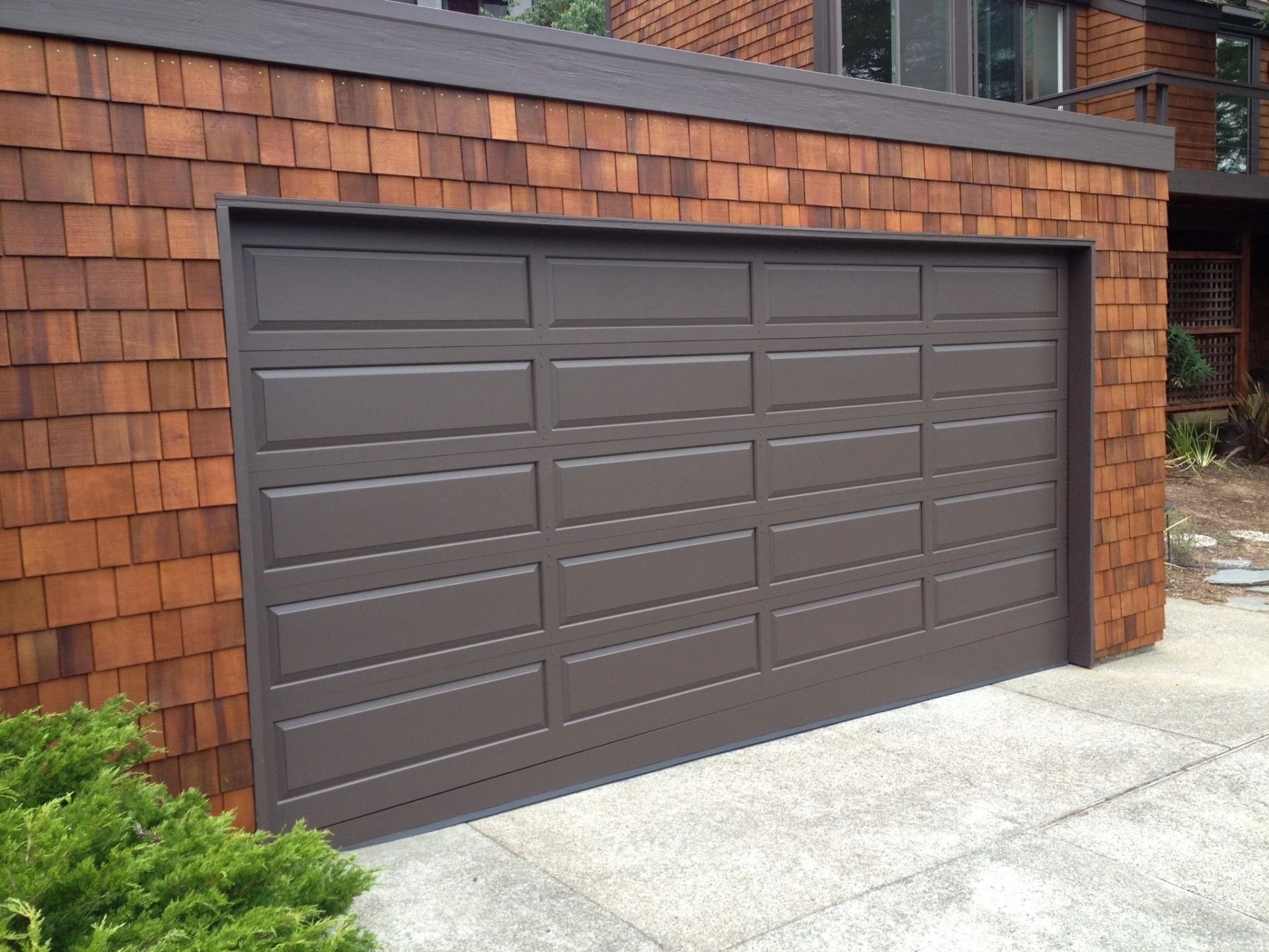 Brown double garage door set into a brick wall beside a concrete driveway