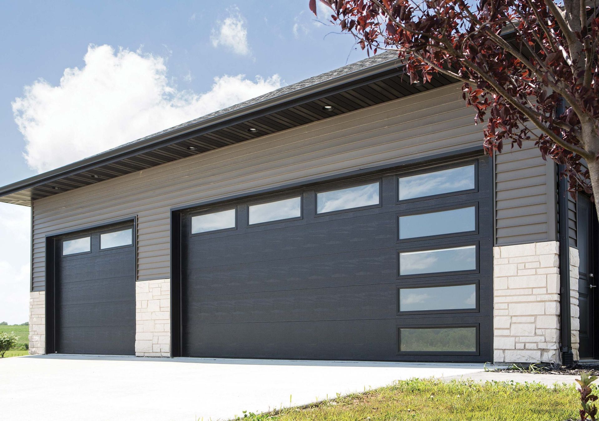 Modern house exterior with two large dark garage doors and light stone siding