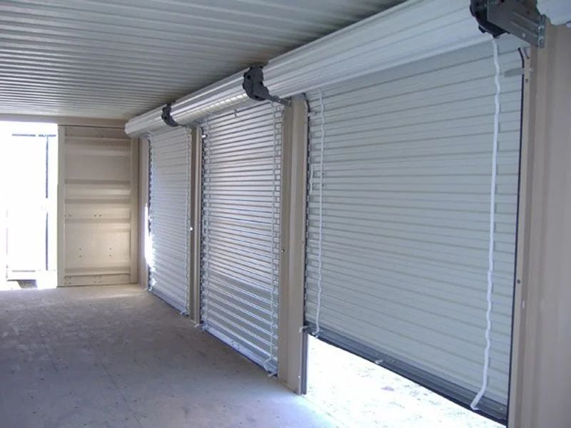Covered walkway with closed white roll-up security doors along the wall
