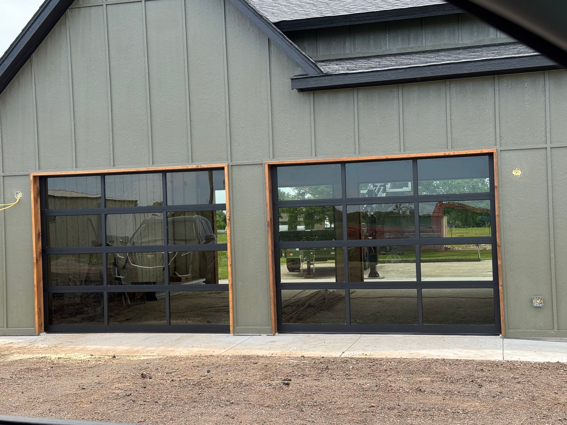 Gray industrial building facade with two large glass garage doors and gravel in front
