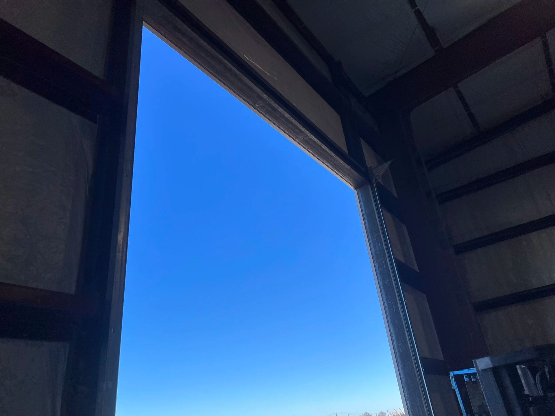 View through an open doorway to a bright blue sky framed by dark beams and walls