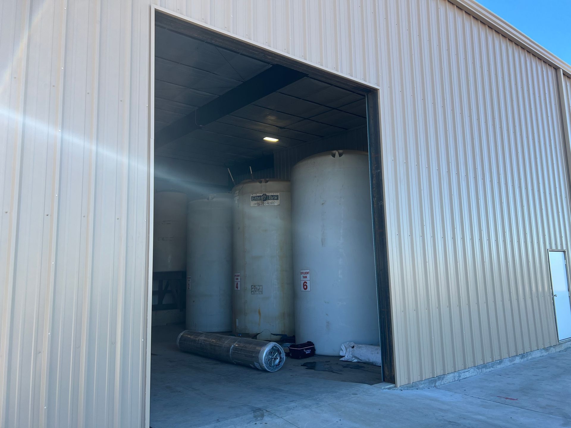 Open warehouse bay with large white industrial storage tanks inside and a pipe on the floor.