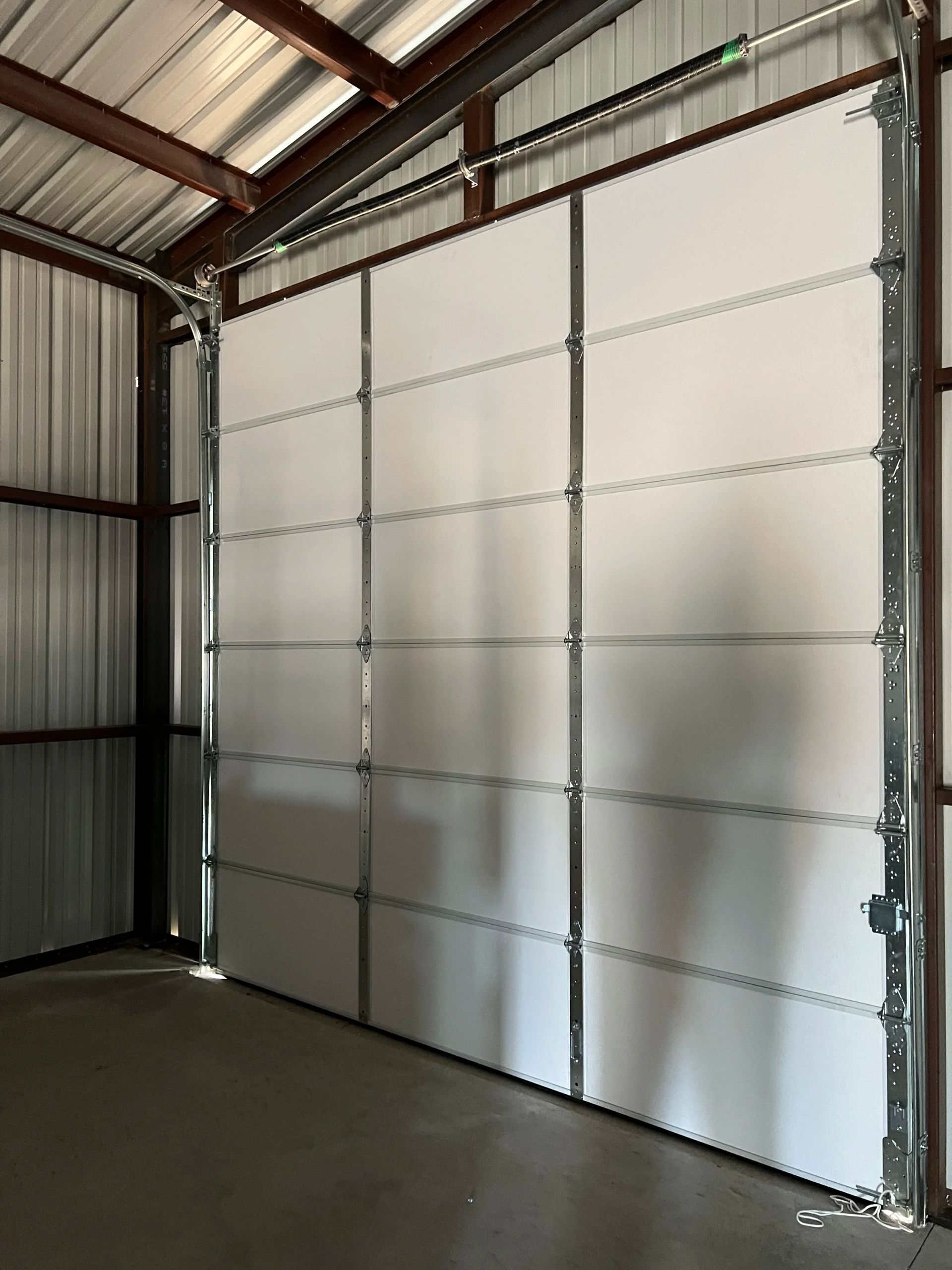 Interior of a metal storage shed with a large white roll-up door and corrugated walls