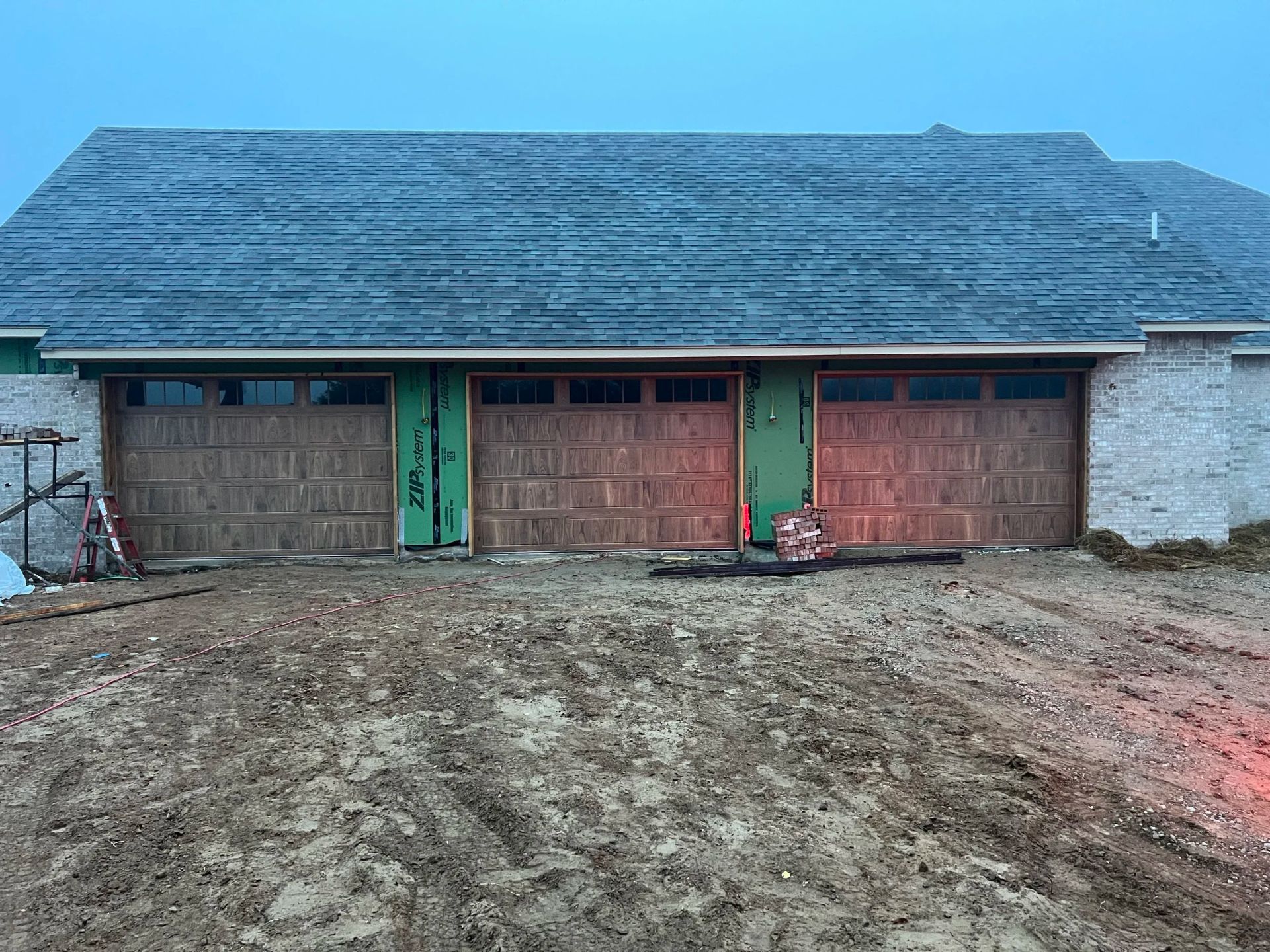 Three-car garage with a weathered roof and muddy driveway in a rural setting