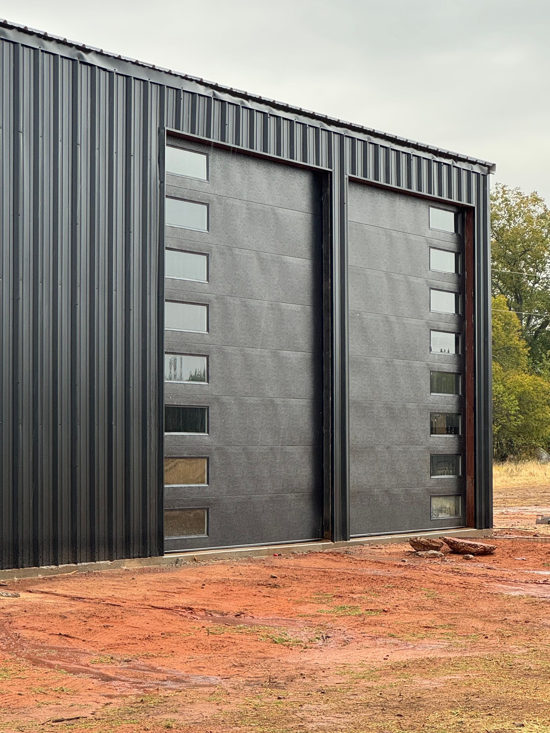 Modern black metal building with large gray sliding doors on a red dirt lot