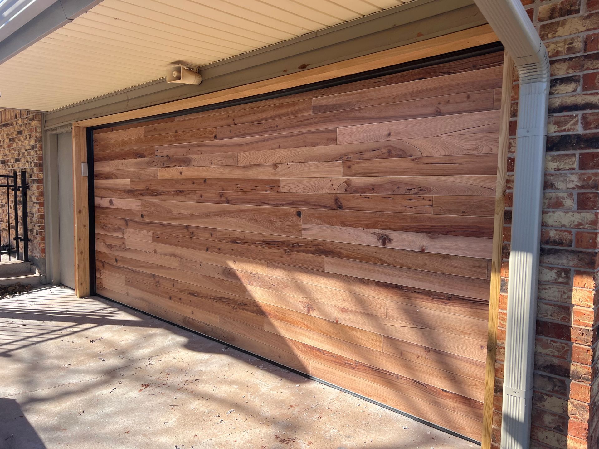 Wood-paneled garage door under a covered driveway beside a brick wall