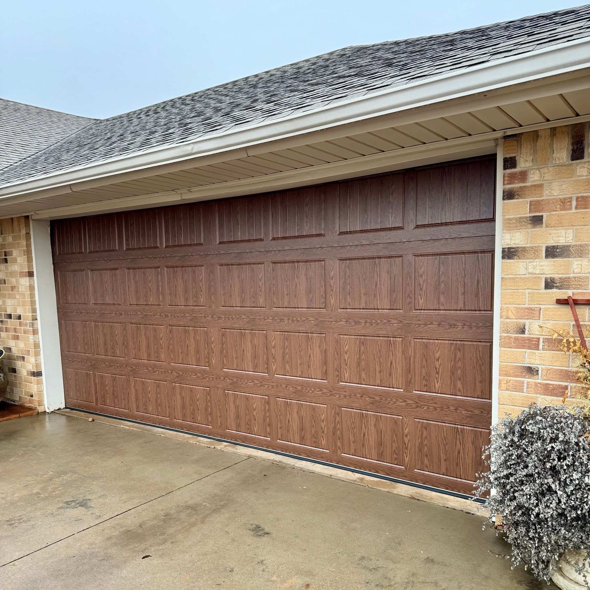 Brown wood-paneled garage door on a brick house with a wet concrete driveway