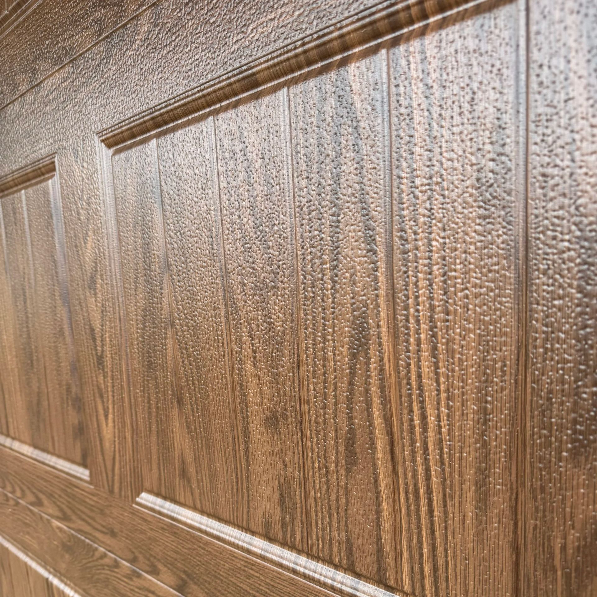 Close-up of a brown wood-paneled door with raised decorative trim and textured grain.