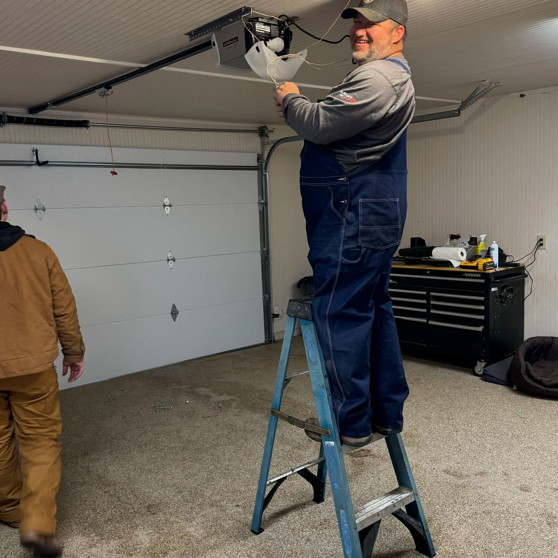 Man standing on a step ladder adjusting a garage door opener in a garage.
