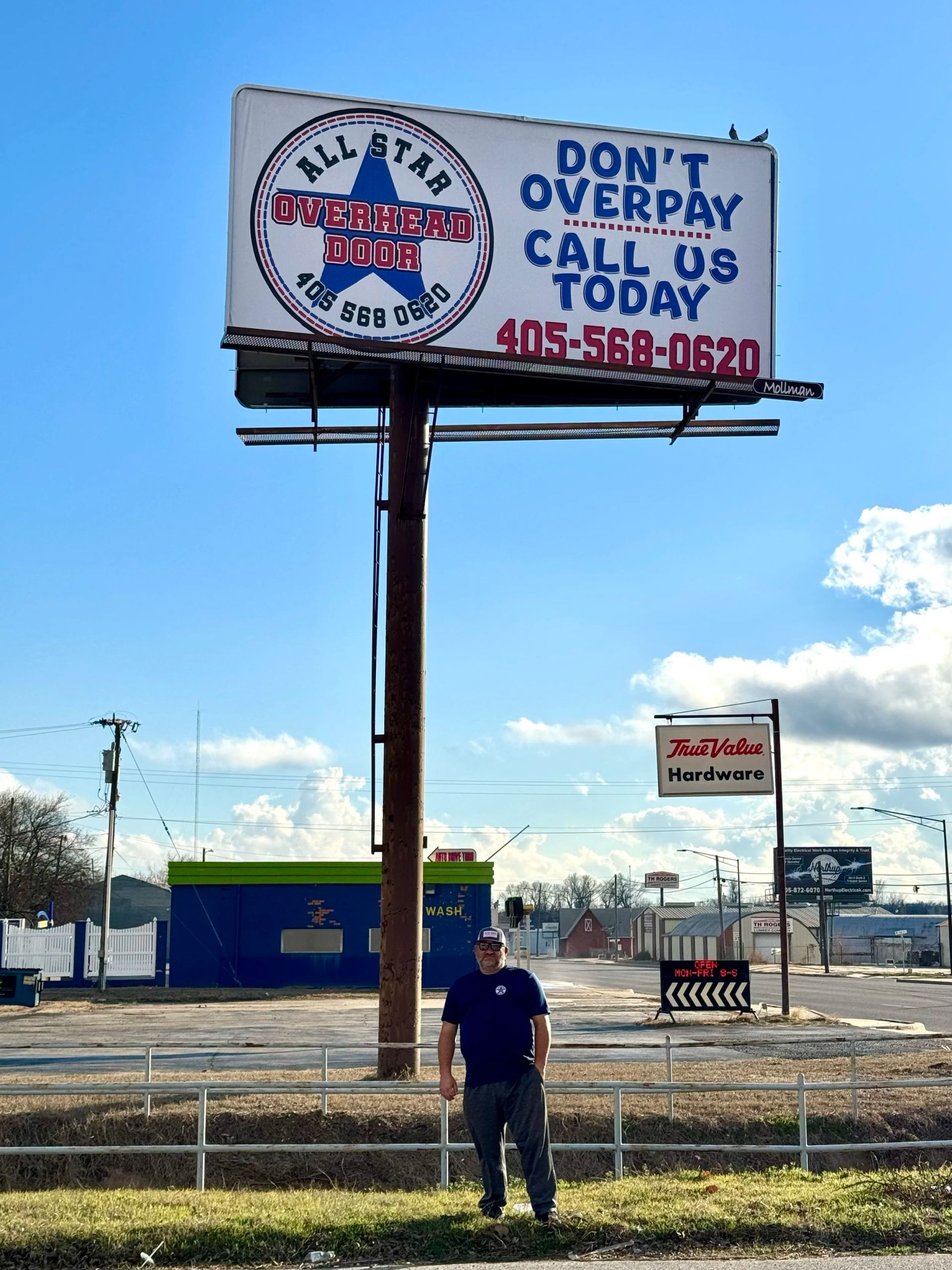 Billboard reading “NO GIMMICKS, NO OVERPAY, CALL TODAY” above a man standing in a lot under a blue sky
