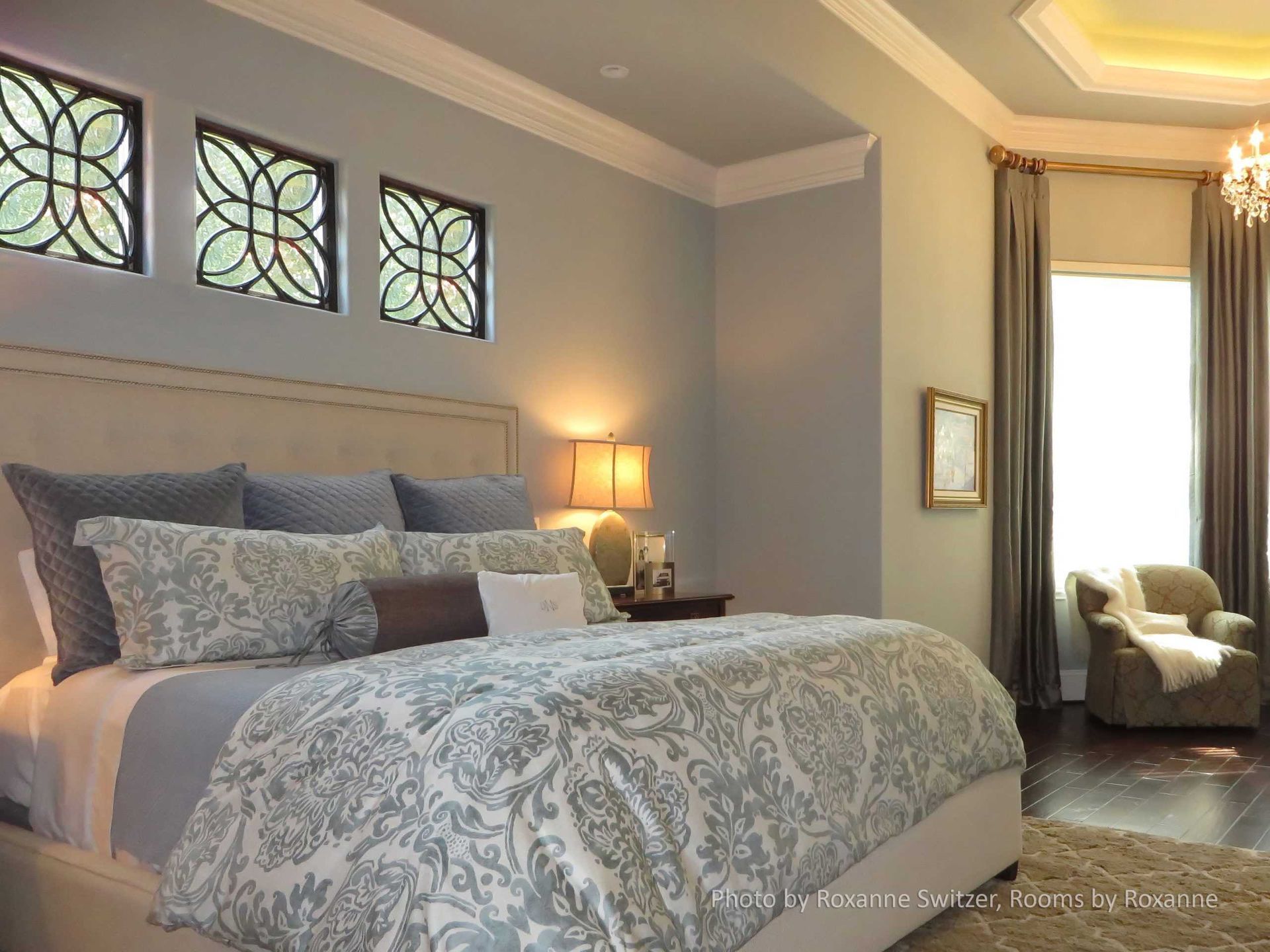Elegant bedroom with a large bed, blue walls, and stained-glass windows, lit by a bedside lamp.
