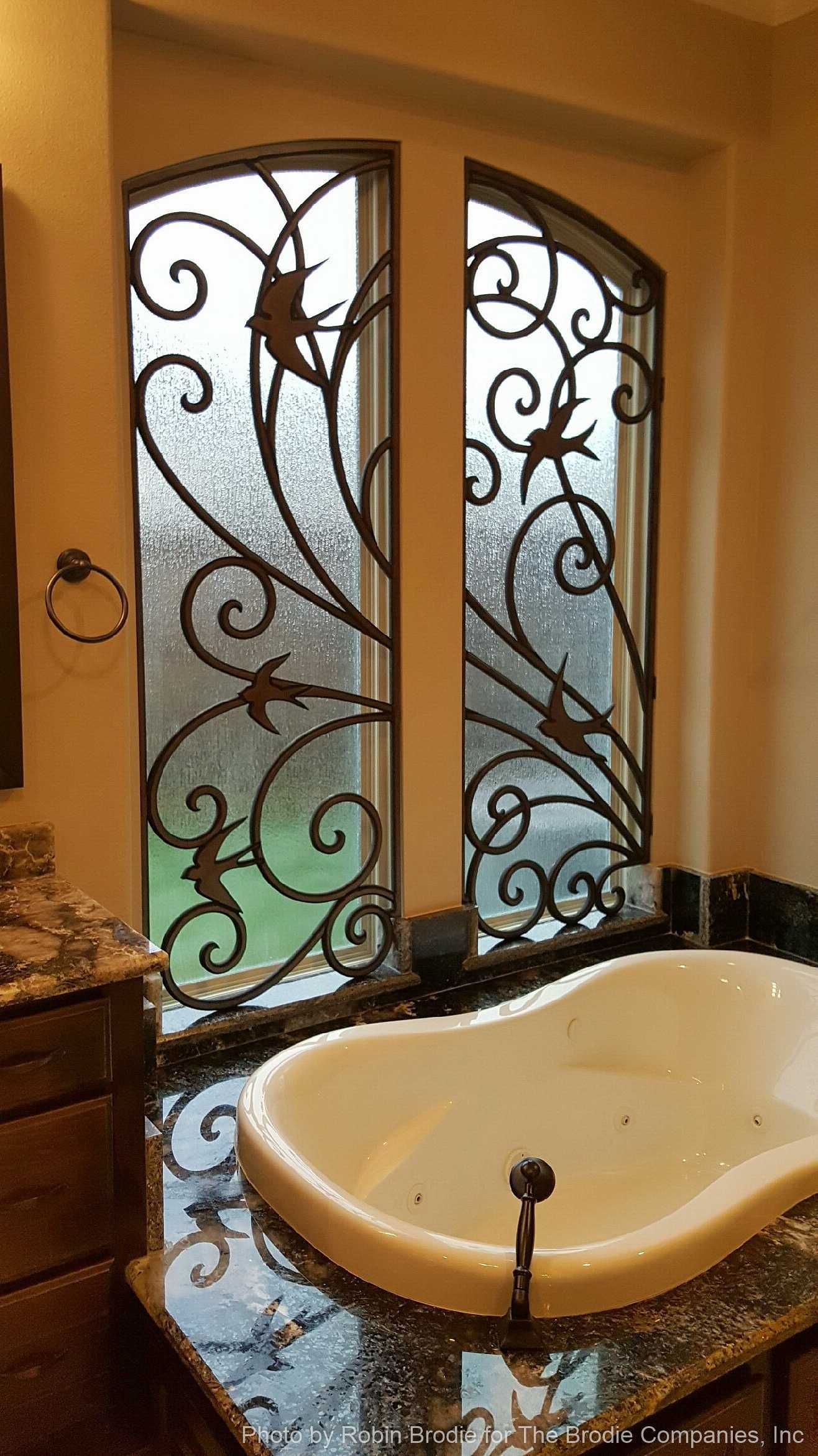 Elegant bathroom with a white sink, ornate wrought-iron window, and warm tan walls