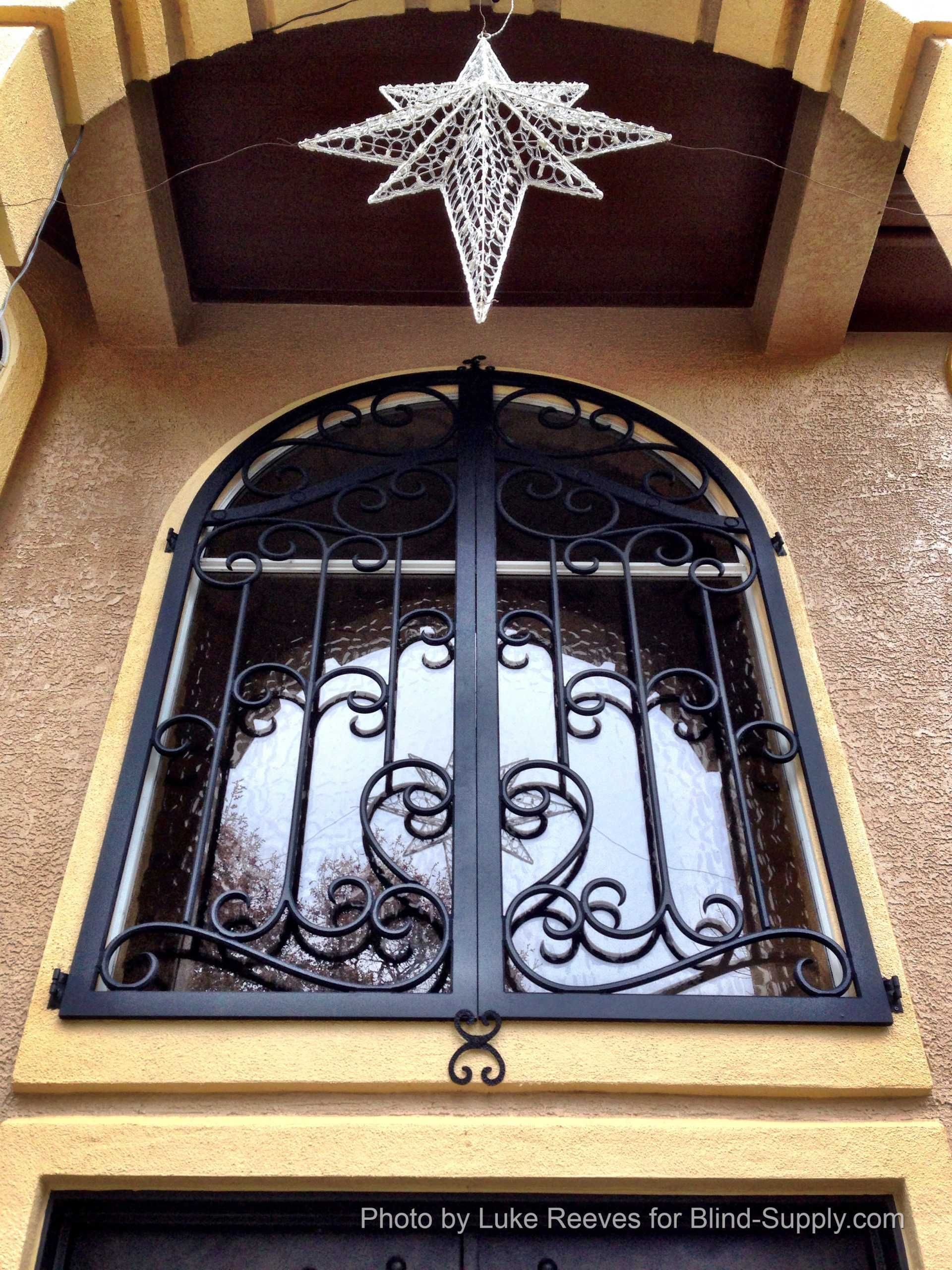 Black wrought-iron arched window gate beneath a white star decoration on a tan building