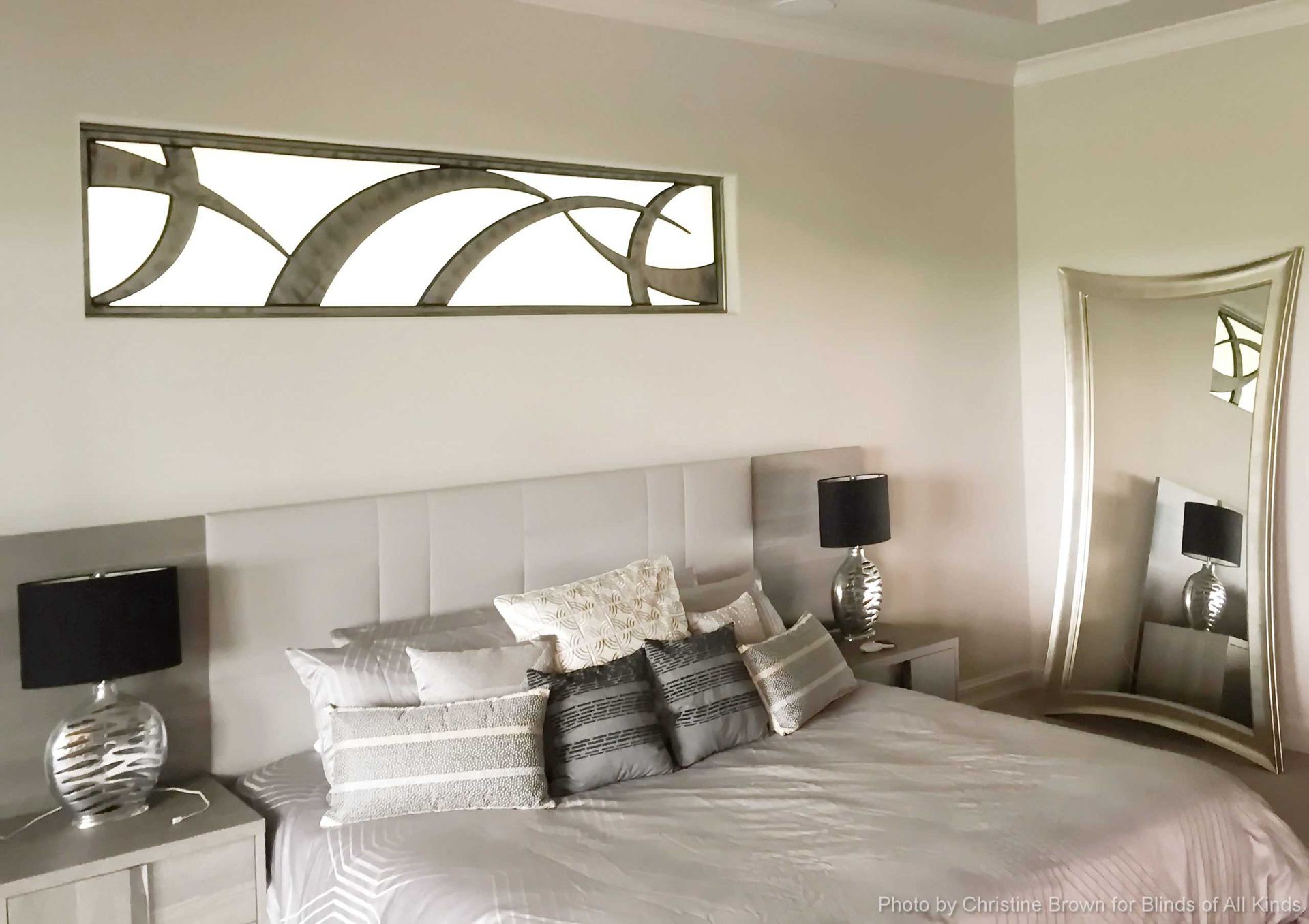 Bright bedroom with a bed, mirrored dresser, and decorative wall art in neutral tones.