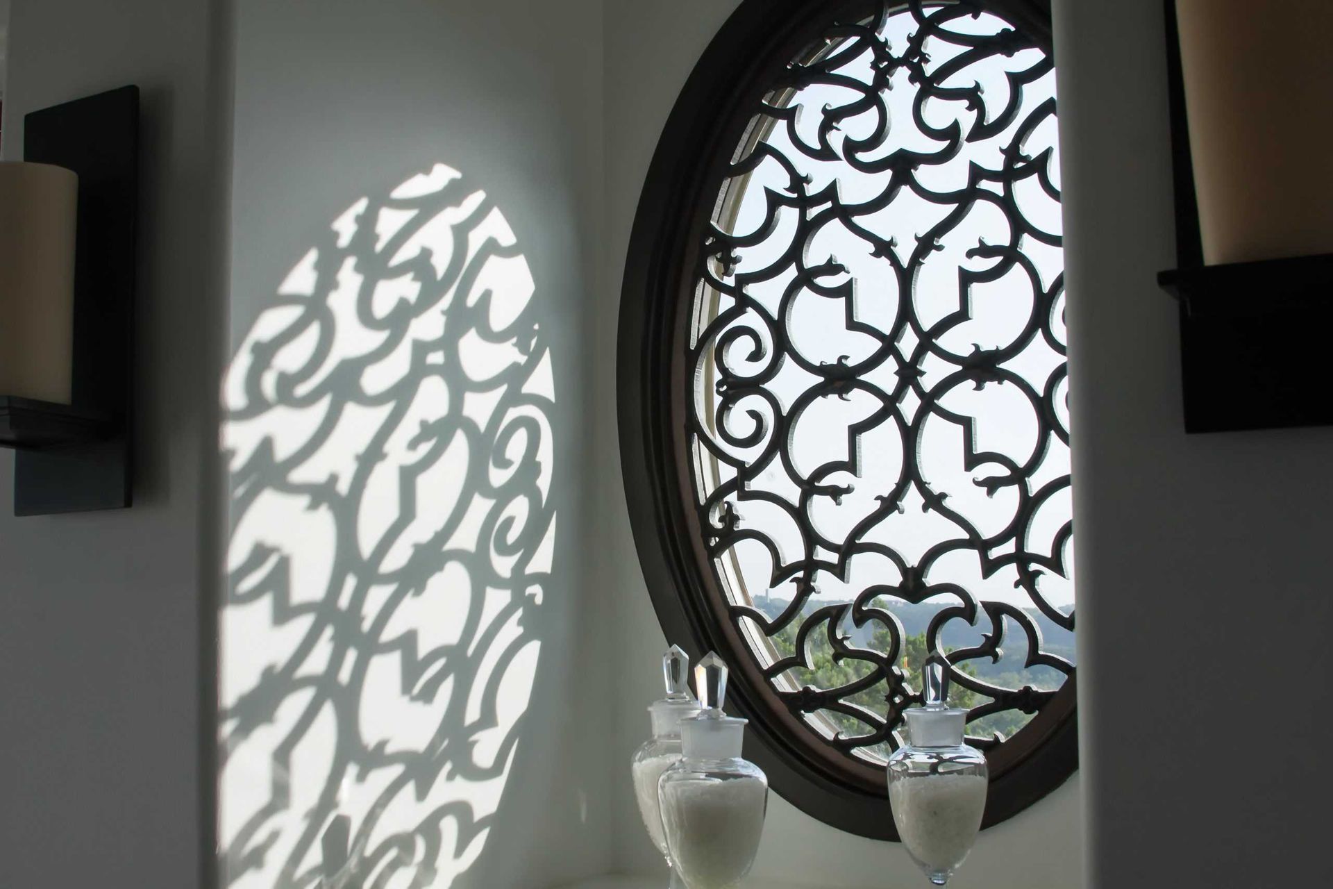 Wall with ornate round window casting patterned light beside white vases on a shelf