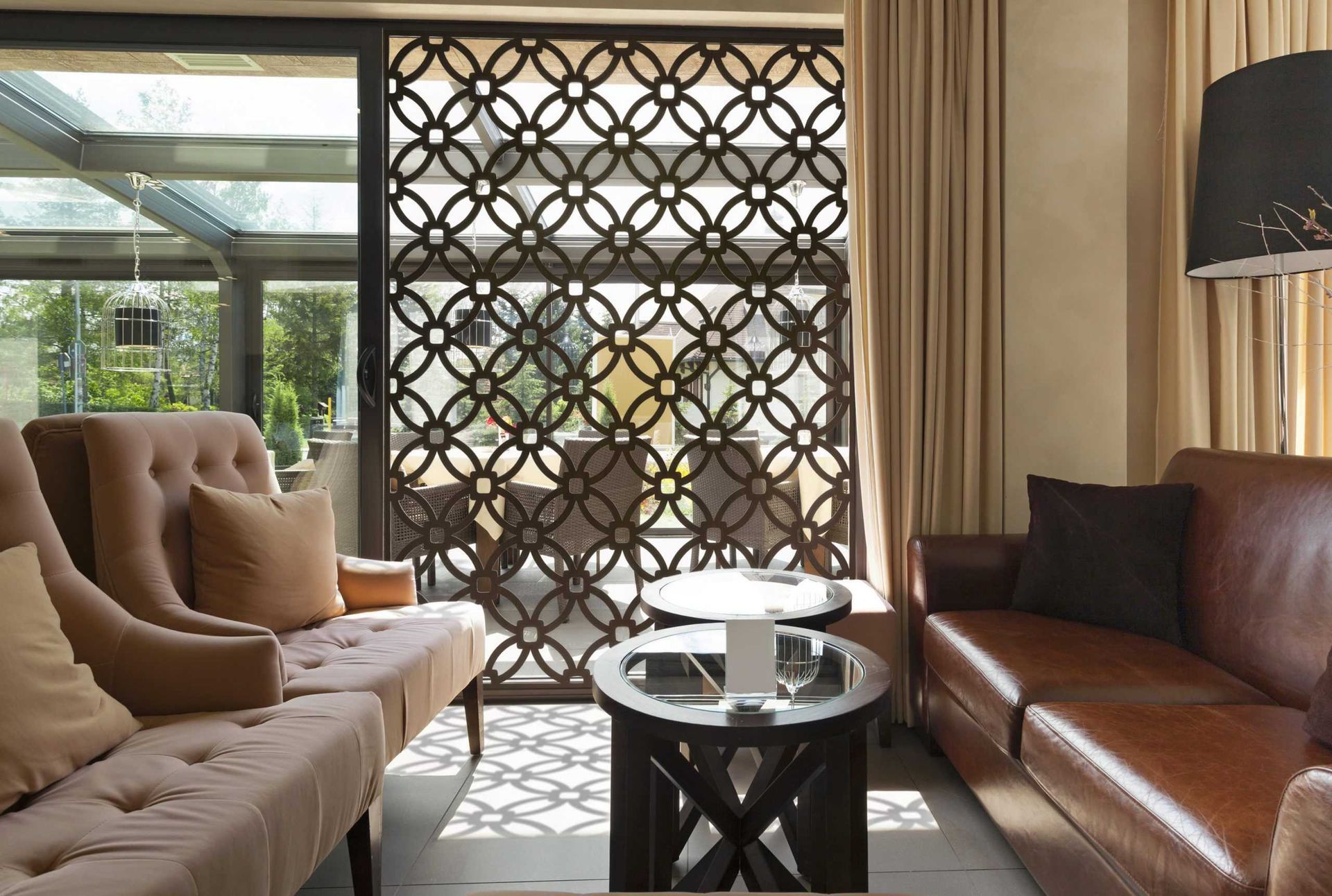 Modern living room with beige and brown sofas, round coffee table, and decorative lattice screen by a window