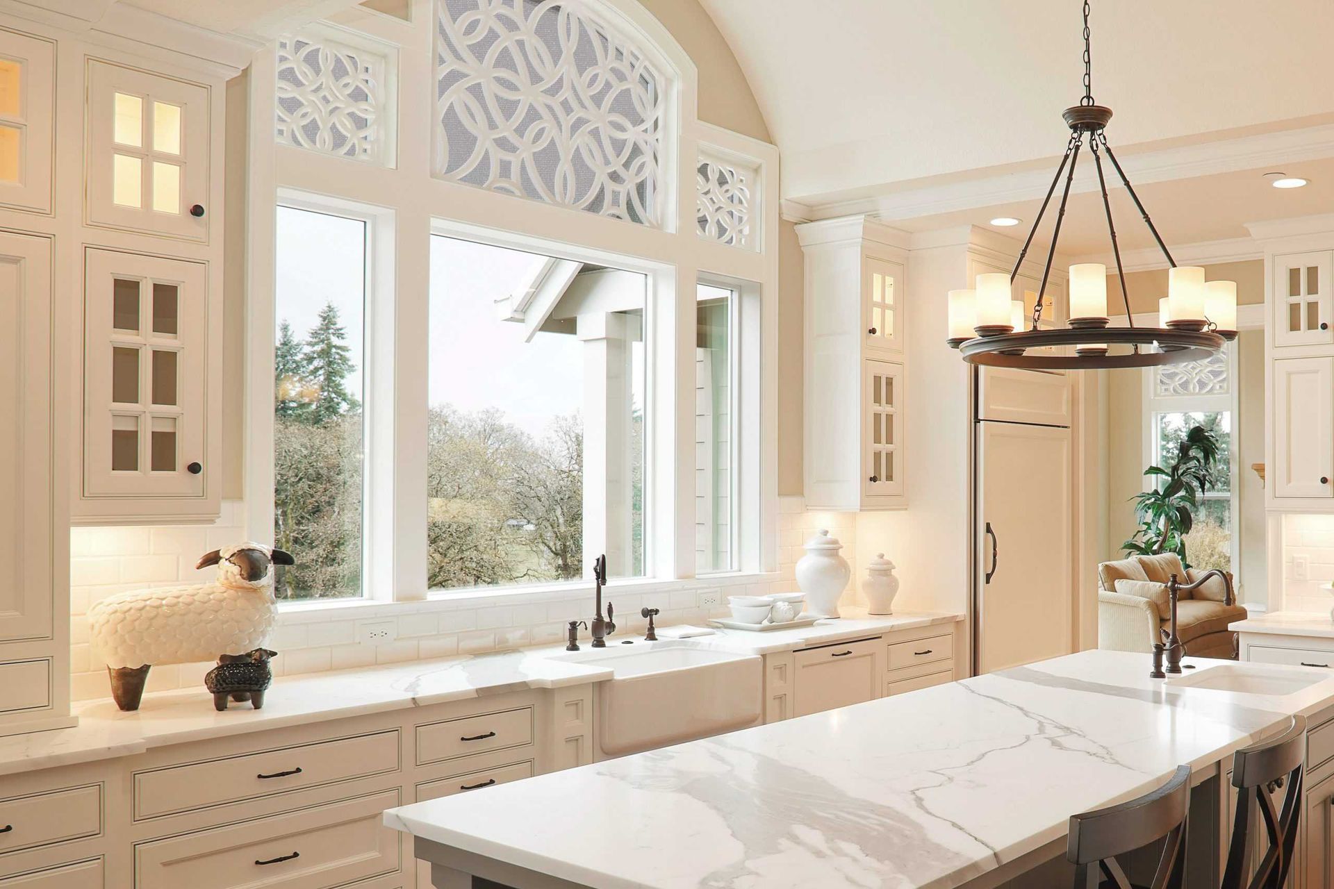Bright white kitchen with large windows, ornate trim, marble island, and modern pendant light