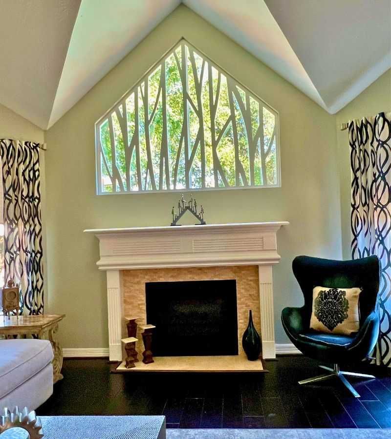Bright living room with vaulted ceiling, tall window, fireplace, and black chair with green pillow.