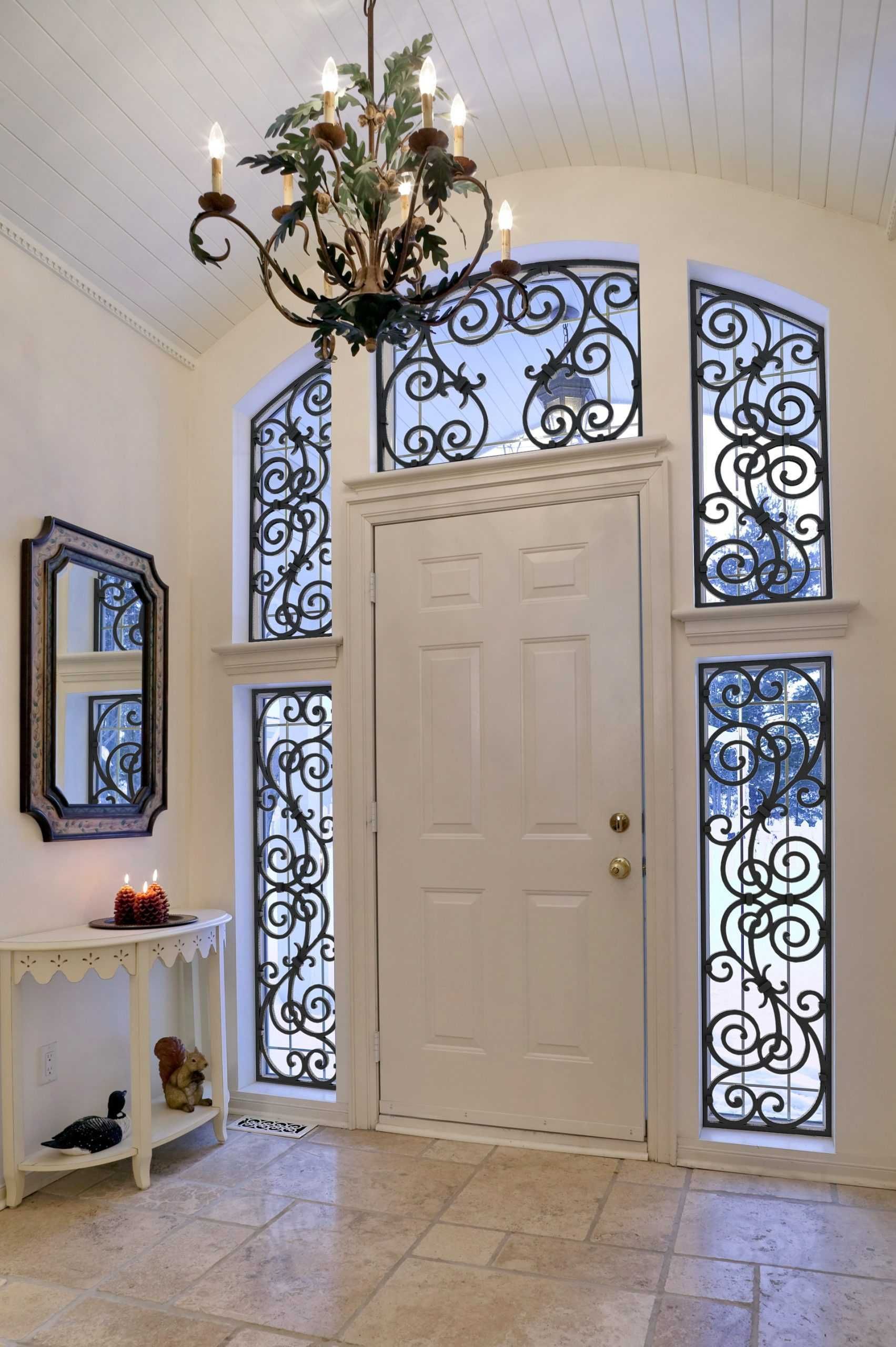 Front door with ornate black wrought-iron panels and chandelier in a white foyer