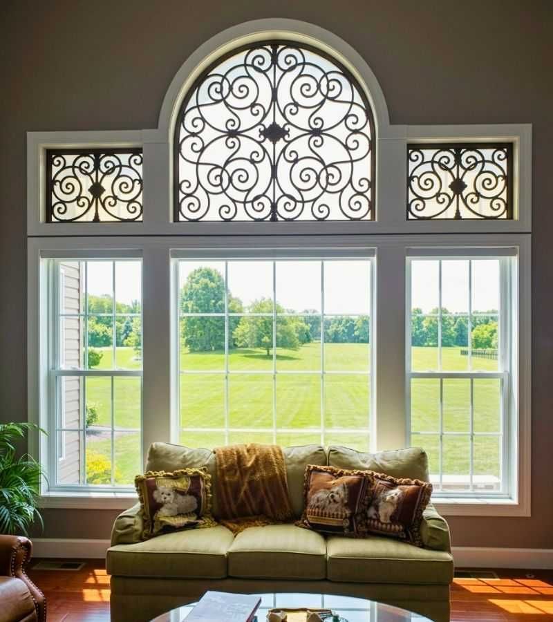 Sunlit living room with a sofa before large ornate windows overlooking a green lawn