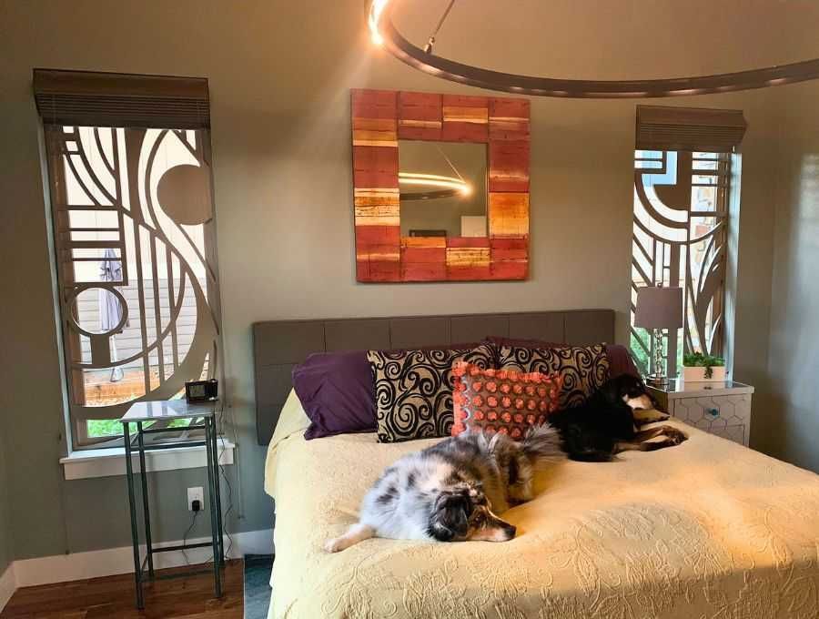 Bedroom with two dogs on a bed, flanked by decorative mirrors and windows with patterned curtains.