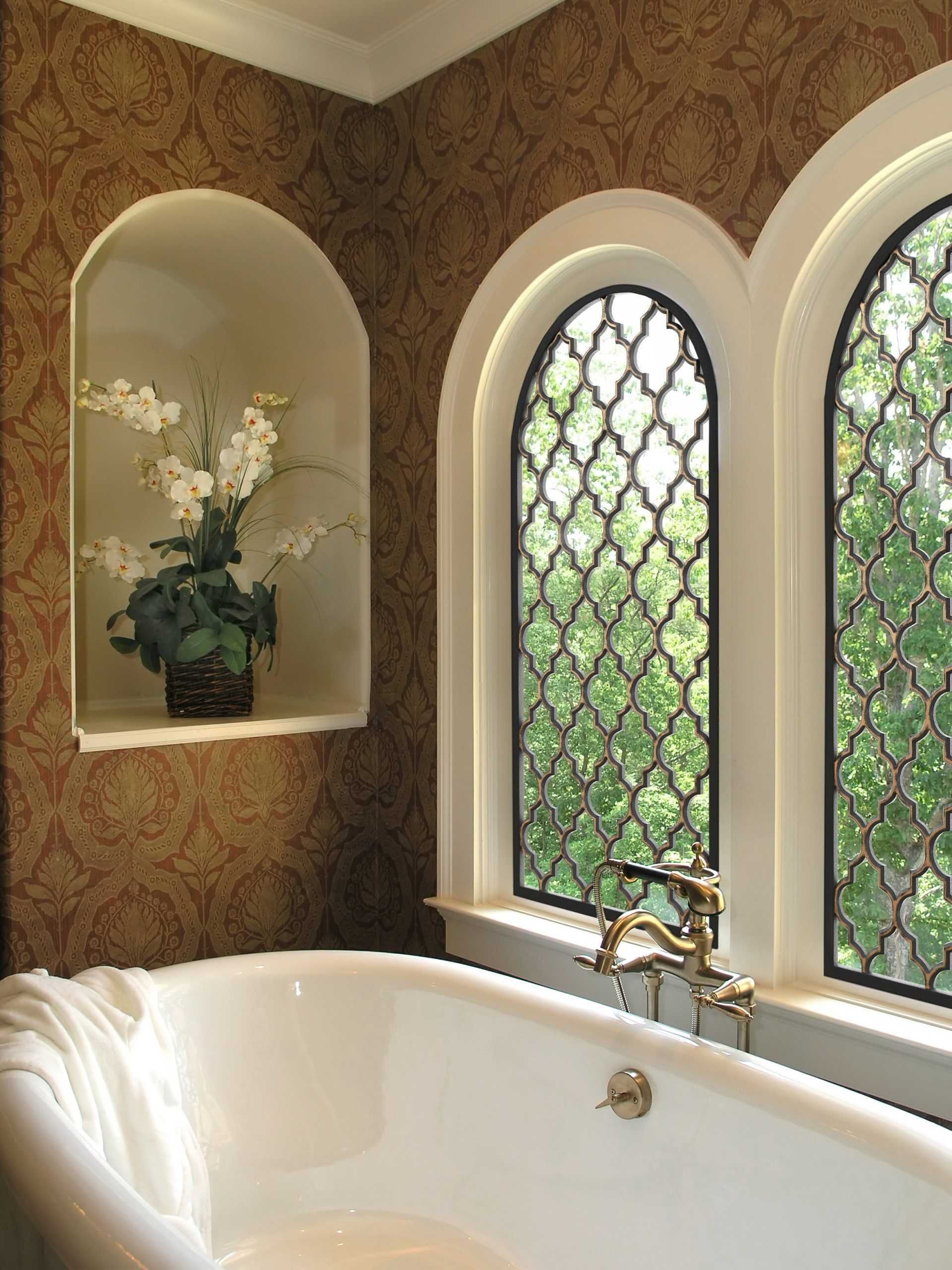 Elegant bathroom with a white tub, arched stained-glass windows, and a built-in alcove with flowers.