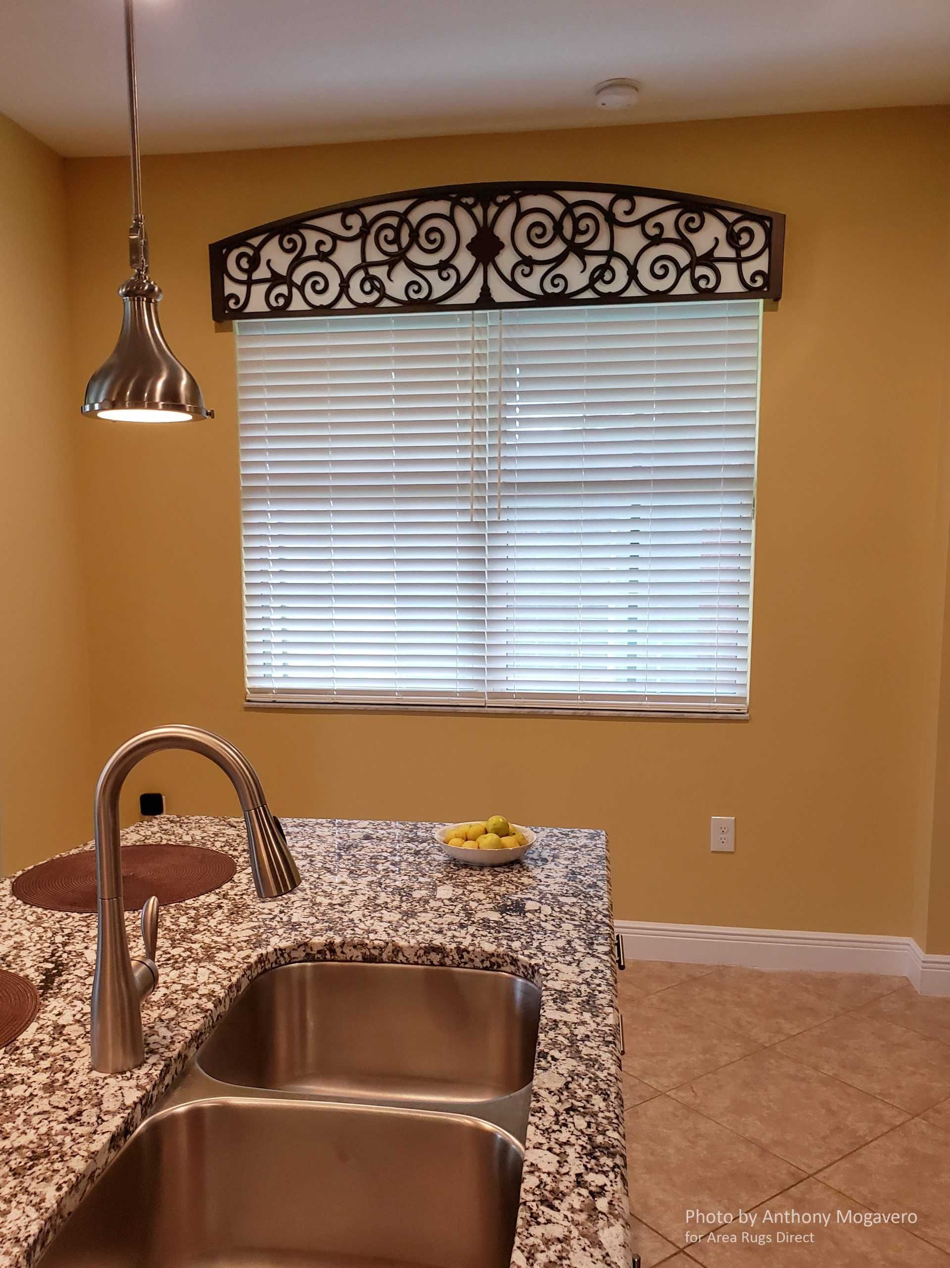 Empty kitchen with tan walls, granite counter, double sink, pendant light, and a window with blinds.