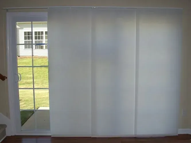 White panel track blinds covering a glass door, revealing a green lawn.