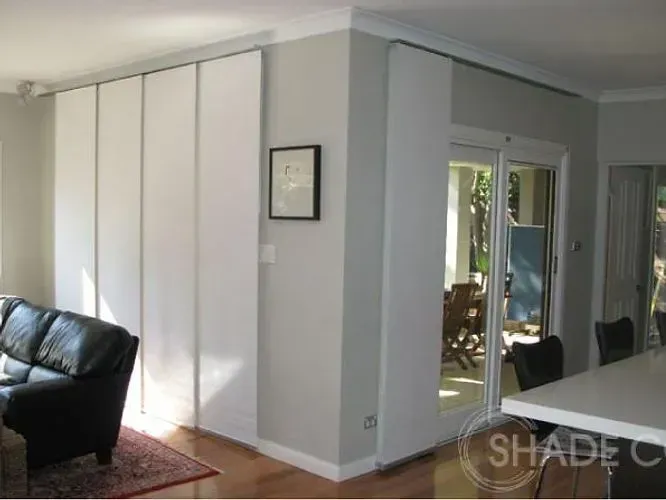 White sliding panel blinds cover a wall in a living room, next to a glass door.