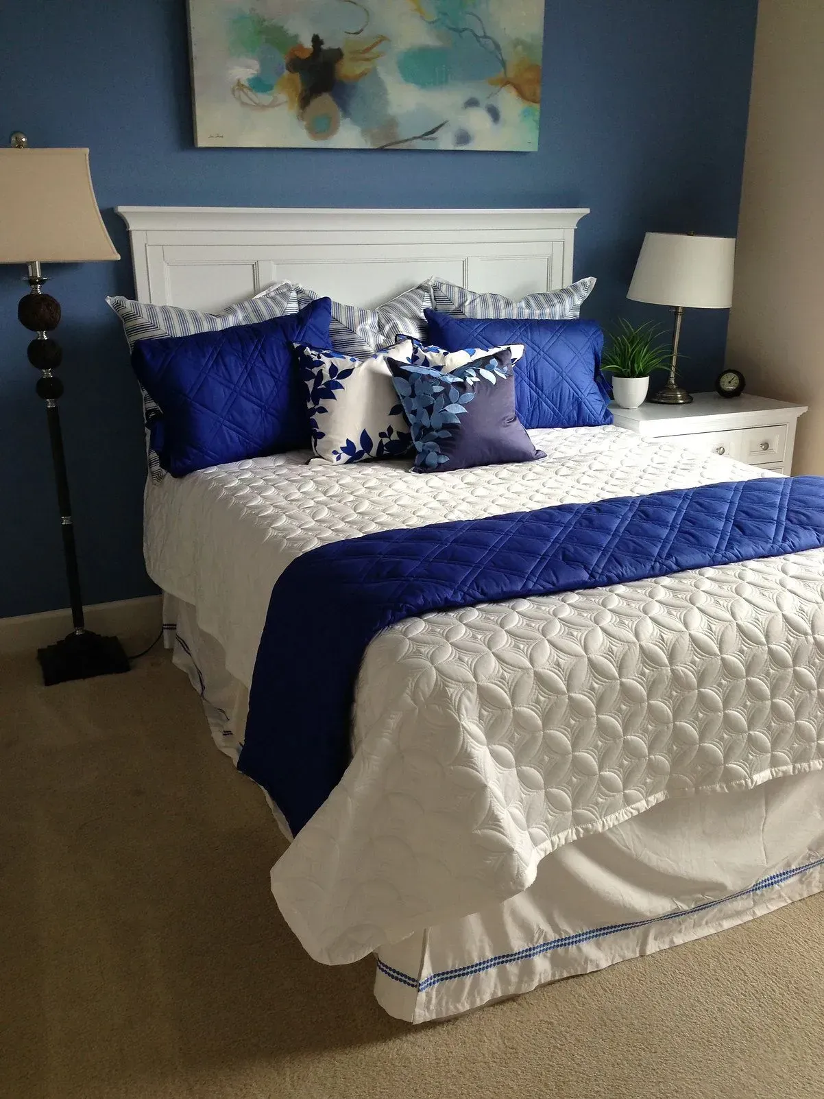 Bedroom with a white bed, blue accents, white nightstand, blue wall, and artwork.