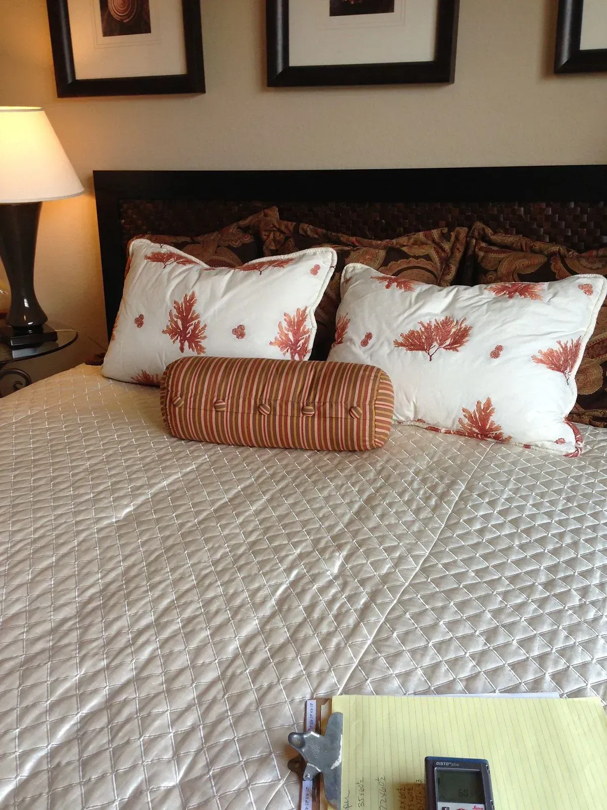Bed with pillows and a bolster; art on the wall above. Beige quilted bedspread.