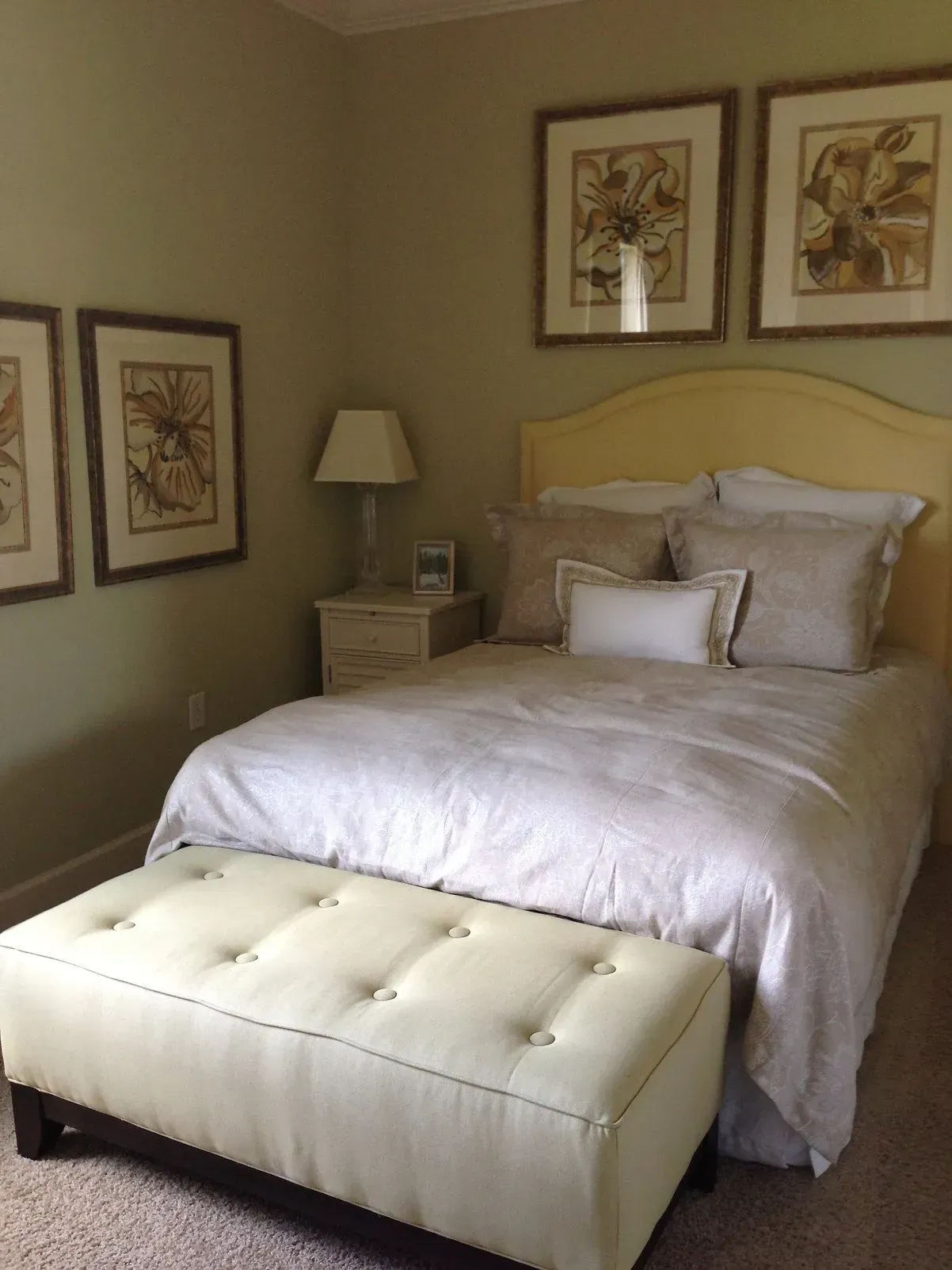 Bedroom with yellow headboard, white bedding, tan bench, and wall art; pale green walls.